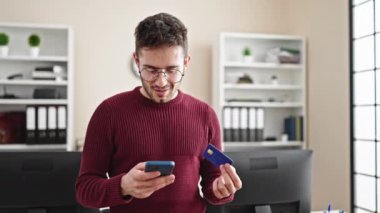 Genç İspanyol iş adamı akıllı telefon ve kredi kartıyla alışveriş yapıyor.