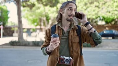 Genç İspanyol turist parkta elinde kahveyle akıllı telefondan konuşuyor.