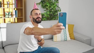 Doğum günü şapkası takan genç İspanyol bir adam evde video görüşmesi yapıyor.