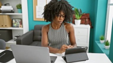 Ofiste rahim ağrısı için dokunmatik ped ve dizüstü bilgisayar kullanan Afrikalı Amerikalı iş kadını.
