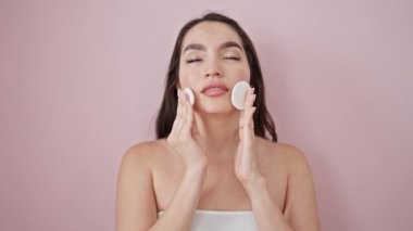 Genç, güzel, İspanyol bir kadın gülümseyen, kendine güvenen, temiz yüzlü, izole pembe arka plan üzerinde pamuk pedler kullanan.