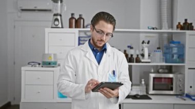 Laboratuvarda gülümseyen dokunmatik ped kullanan genç İspanyol bilim adamı.