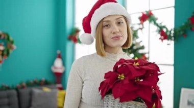 Genç sarışın kadın elinde Noel çiçeği tutuyor.
