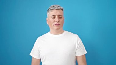 Kafkas 'lı genç adam, izole edilmiş mavi arka planda kızgın yüzüyle boşluğu işaret ediyor.