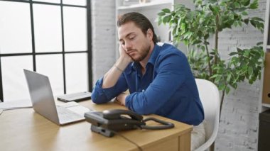 Genç İspanyol iş adamı ofiste dizüstü bilgisayar kullanıyor.