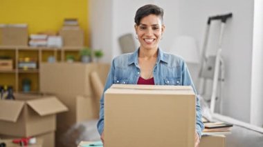 Young beautiful hispanic woman smiling confident holding package at new home
