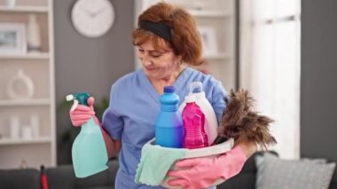 Orta yaşlı kadın profesyonel temizlikçi elinde temiz ürünlerle dolu sepeti tutuyor.