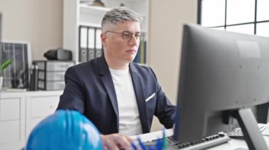 Kafkasyalı genç iş adamı bilgisayarı kullanıyor. Ofiste kollarını kavuşturup gülümsüyor.