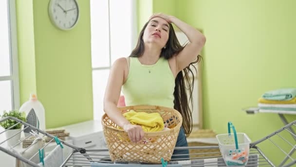 若い美しいヒスパニック女性は 洗濯室で疲れた服でバスケットを持っています — ストック動画