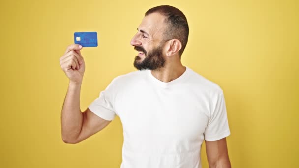 年轻的他的惊慌失措的男人微笑着 自信地拿着信用卡 带着胜利的手势 而不是孤立的黄色背景 — 图库视频影像