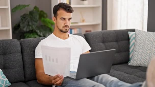Jonge Spaanse Man Met Behulp Van Laptop Lezen Papier Thuis — Stockvideo