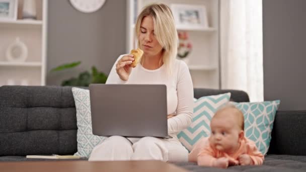 自宅で一緒に座っているクロワッサンを食べるラップトップを使用して母と娘 — ストック動画