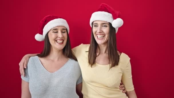 Dos Mujeres Abrazándose Usando Sombrero Navidad Sobre Fondo Rojo Aislado — Vídeos de Stock