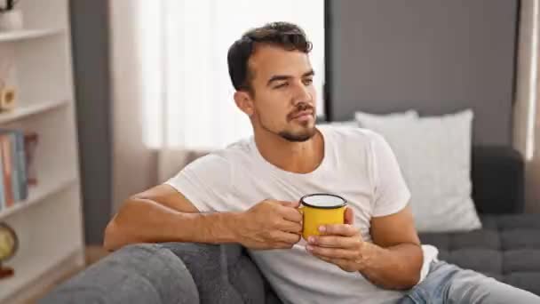 Jonge Spaanse Man Die Thuis Koffie Drinkt Zittend Bank — Stockvideo