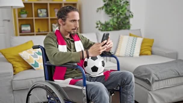 自宅で車椅子に座っているスマートフォンでサッカーを見ている若いヒスパニック男性 — ストック動画