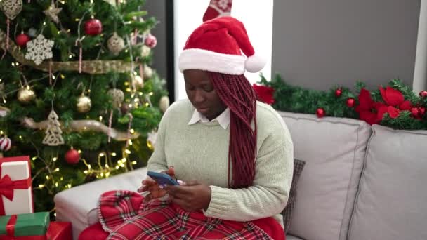 Αφρικανική Γυναίκα Πλεγμένα Μαλλιά Χρησιμοποιώντας Smartphone Κάθεται Από Χριστουγεννιάτικο Δέντρο — Αρχείο Βίντεο
