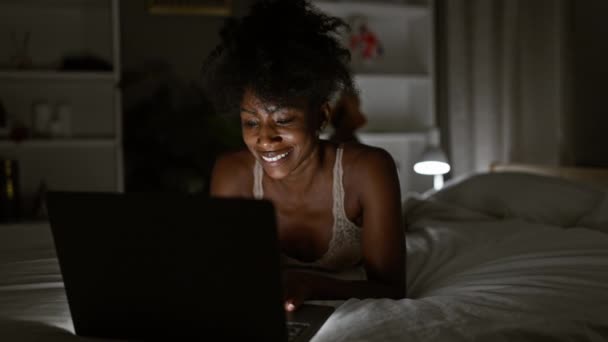 アフリカ系アメリカ人女性は寝室でベッドに横たわるラップトップを使用してランジェリーを着用しています — ストック動画