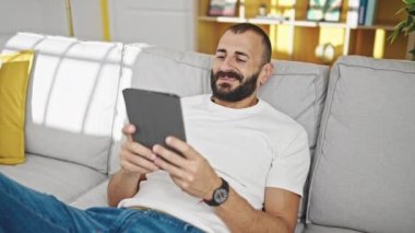 Genç İspanyol adam evdeki koltukta otururken dokunmatik ped kullanıyor.