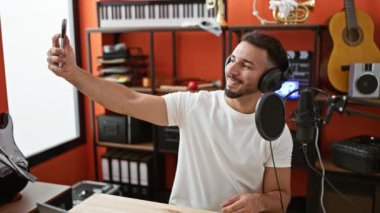 Kulaklık takan genç Arap müzisyen müzik stüdyosunda akıllı telefondan selfie çekiyor.