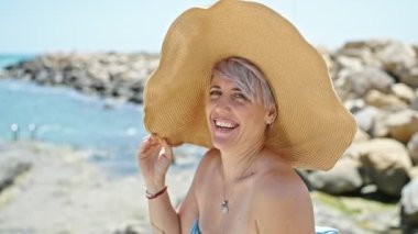 Bikini giyen ve plajda gülümseyen genç bir kadın turist.