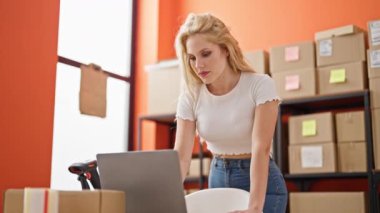 Genç sarışın iş kadını ofisteki dizüstü bilgisayarını kullanarak gülümsüyor.