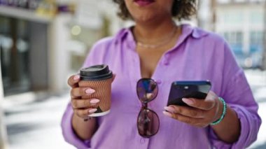 Genç, güzel, Latin bir kadın. Elleri boşta. Elinde kahve tutuyor.