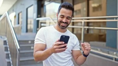 Genç İspanyol adam dans ediyor, sokakta akıllı telefondan müzik dinliyor.