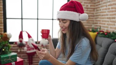 Genç ve güzel İspanyol kadın akıllı telefon kullanıyor. Evde Noel 'i kutlamak için kahve içiyor.