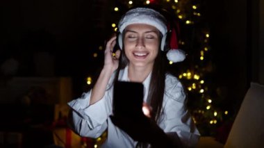 Genç, güzel, İspanyol bir kadın telefon kullanıyor. Evde Noel 'i kutlamak için müzik dinliyor.