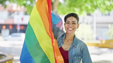 Parkta gökkuşağı bayrağı tutan güzel İspanyol kadın gülümsüyor.