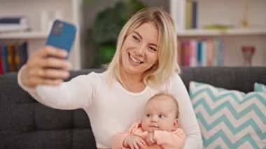 Anne ve kızı birbirlerine sarılıyorlar ve evde akıllı telefondan selfie çekiyorlar.
