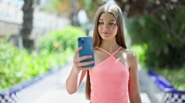 Genç ve güzel bir kız. Parktaki akıllı telefonun yanında kendinden emin bir şekilde selfie çekiyor.