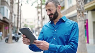 Young hispanic man smiling confident using touchpad at street