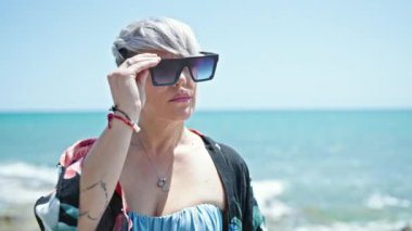 Bikini giyen ve plajda gülümseyen güneş gözlüklü genç bir kadın turist.