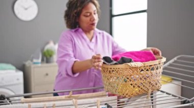 Genç ve güzel Latin kadın gülümsüyor. Çamaşır odasında çamaşır ipine asılan kendine güveni tam.