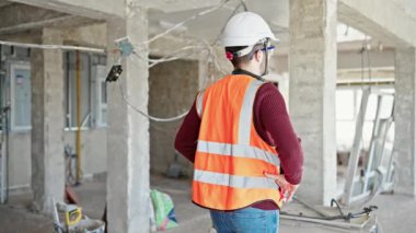 İspanyol asıllı genç inşaatçı gülümsüyor. Şantiyede kollarını kavuşturup duruyor.
