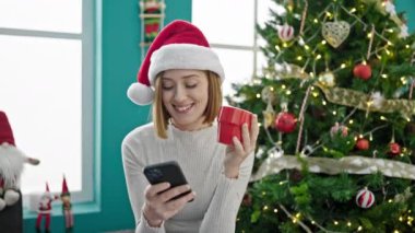 Genç sarışın kadın akıllı telefon kullanıyor evde Noel 'i kutlamak için kahve içiyor.