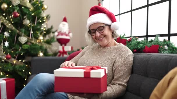 Frau Mittleren Alters Mit Grauen Haaren Trägt Weihnachtsmütze Beim Auspacken — Stockvideo