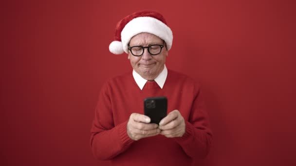 Senior Con Sombrero Navidad Apuntando Teléfono Inteligente Sobre Fondo Rojo — Vídeo de stock