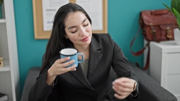 若い美しいヒスパニック系女性ビジネスワーカーがオフィスでコーヒーを飲むのを見ている — ストック動画