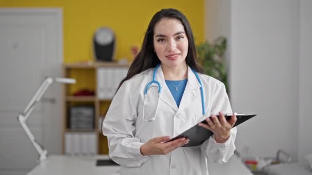 年轻美丽的惊慌失措的女医生牵着剪贴板在诊所微笑 — 图库视频影像