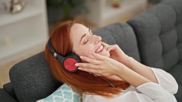 Młoda Ruda Kobieta Słucha Muzyki Siedząc Kanapie Domu — Wideo stockowe