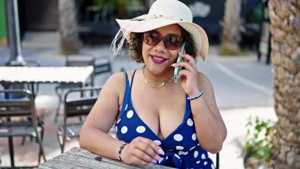 年轻美丽的拉丁女游客戴着夏帽和太阳镜 在咖啡店的阳台上用智能手机交谈 — 图库视频影像