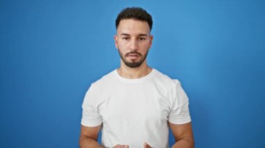 Genç Arap adam gülümsüyor, kendinden emin, soyutlanmış mavi arka planda konuşuyor.