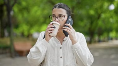 Genç, güzel İspanyol kadın telefonda konuşuyor. Parkta kahve içiyor.