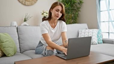 Dizüstü bilgisayar kullanan genç bir kadın evinde karın ağrısı çeken bir koltukta oturuyor.