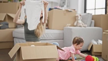 Anne ve kızı yeni evlerinde yerde oynayan karton kutuları paketliyor.