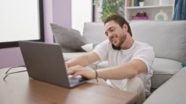 Genç İspanyol adam akıllı telefonda dizüstü bilgisayar kullanarak konuşuyor evde oturuyor.