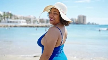 Genç ve güzel Latin kadın turist gülümsüyor. Mayolu ve plajda yaz şapkası takıyor.