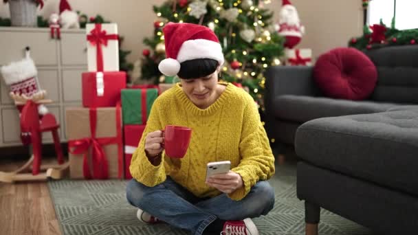 Jovem Chinesa Usando Smartphone Bebendo Café Pela Árvore Natal Casa — Vídeo de Stock
